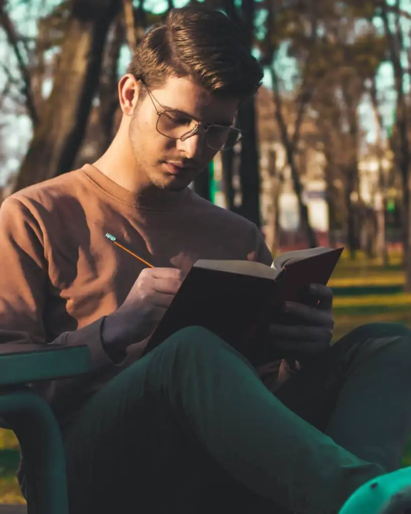 A man sitting in nature reading a book about advanced caping techniques.